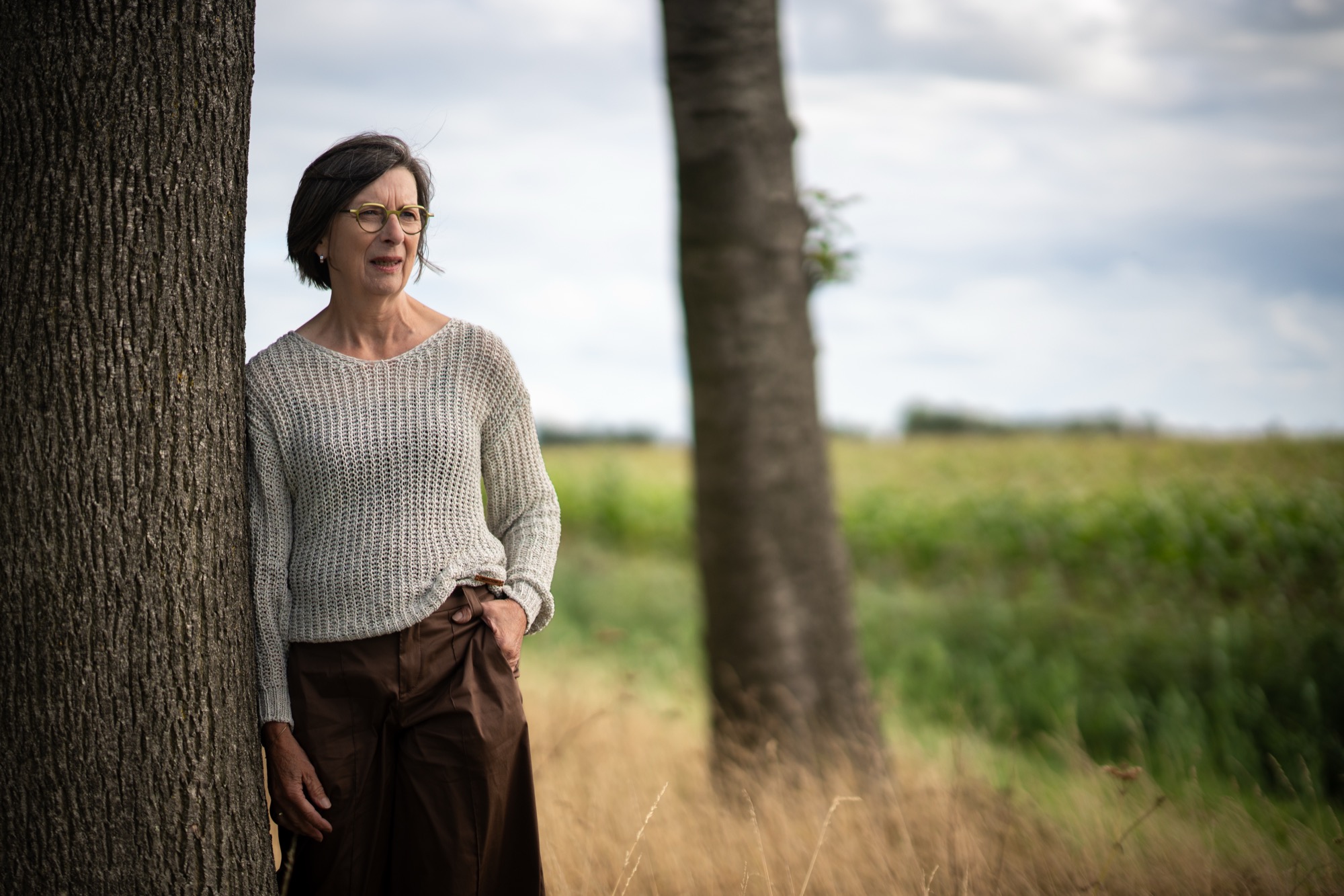 Rita van der Laag leunt tegen een boom aan de rand van een veld